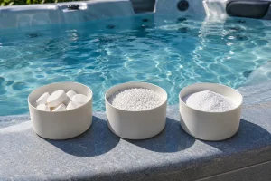 Trois bols alignés sur le rebord d’une piscine spa, chacun contenant des produits de désinfection blancs de formes